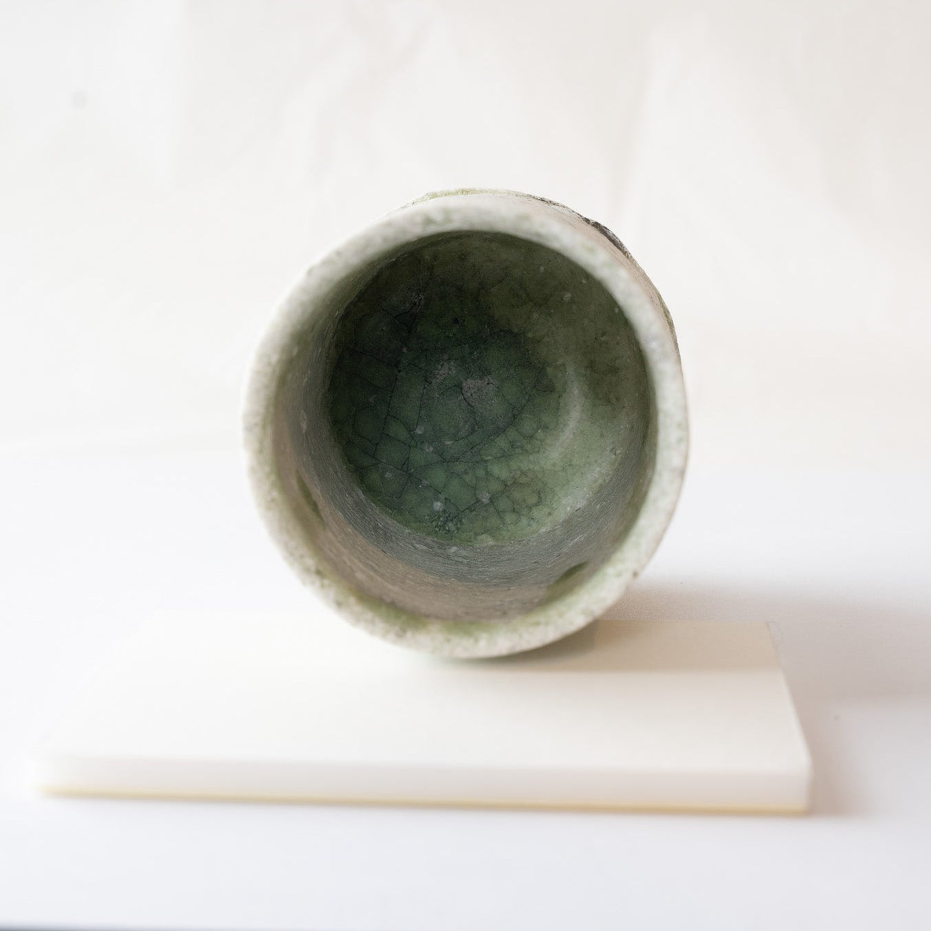 Interior view looking into the bottom of Yui Tsujimura’s YUNOMI cup, displaying a thick pool of deep green glass glaze with delicate crackle patterns.