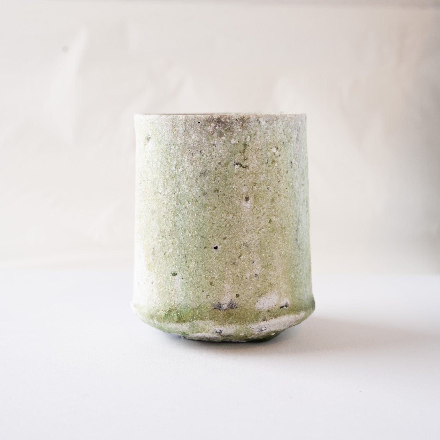 Low-angle view of the natural ash glaze YUNOMI cup by Yui Tsujimura, emphasizing the straight form, stable base, and organic glaze coloration.
