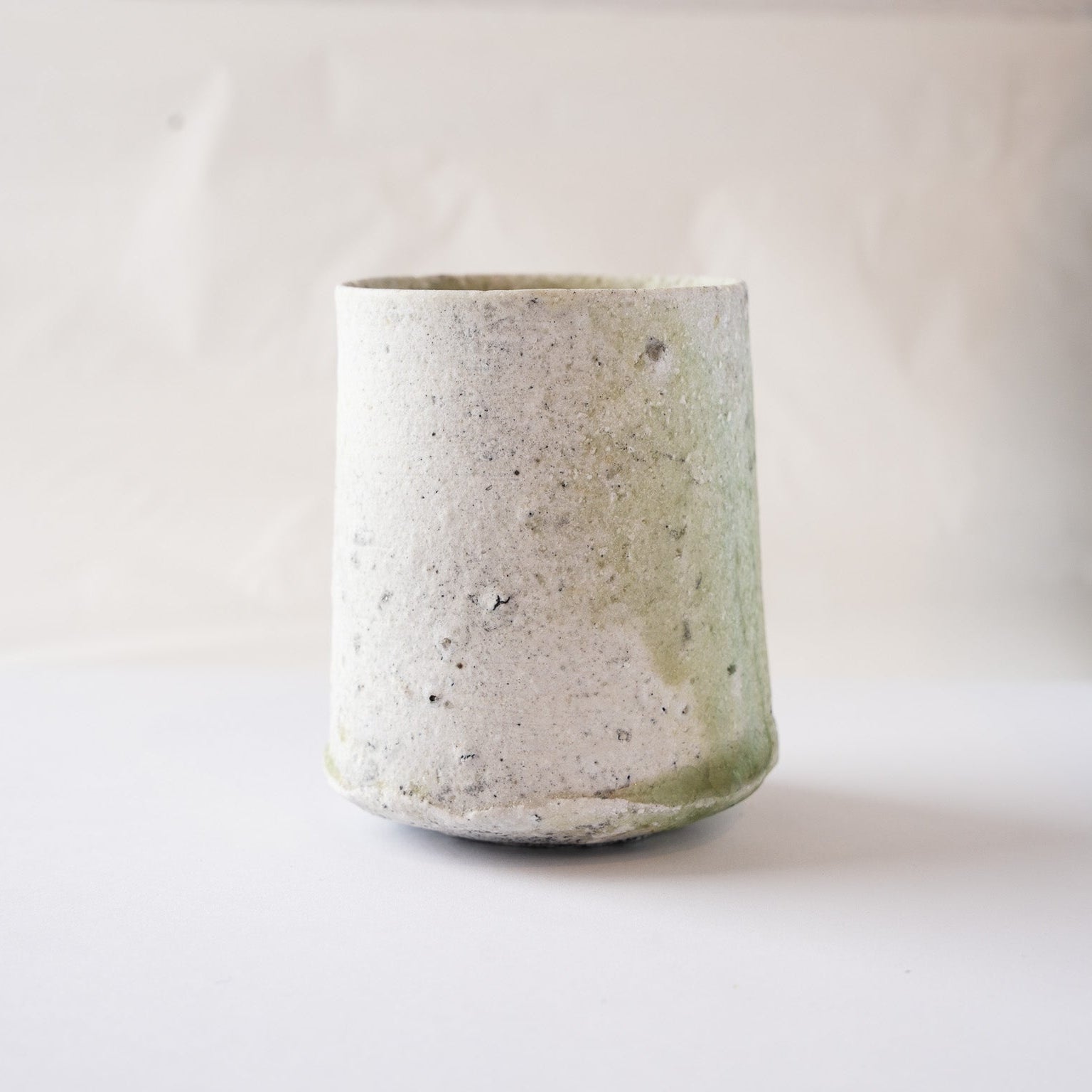 Rear profile of Yui Tsujimura’s YUNOMI ceramic tea cup, showing the subtle transition from the textured white surface to the green glaze at the edge.