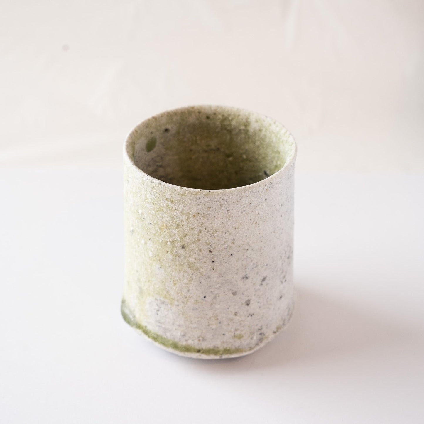 Three-quarter view from the white side of Yui Tsujimura's YUNOMI cup, highlighting the understated elegance and earthy texture of the vessel's rim.
