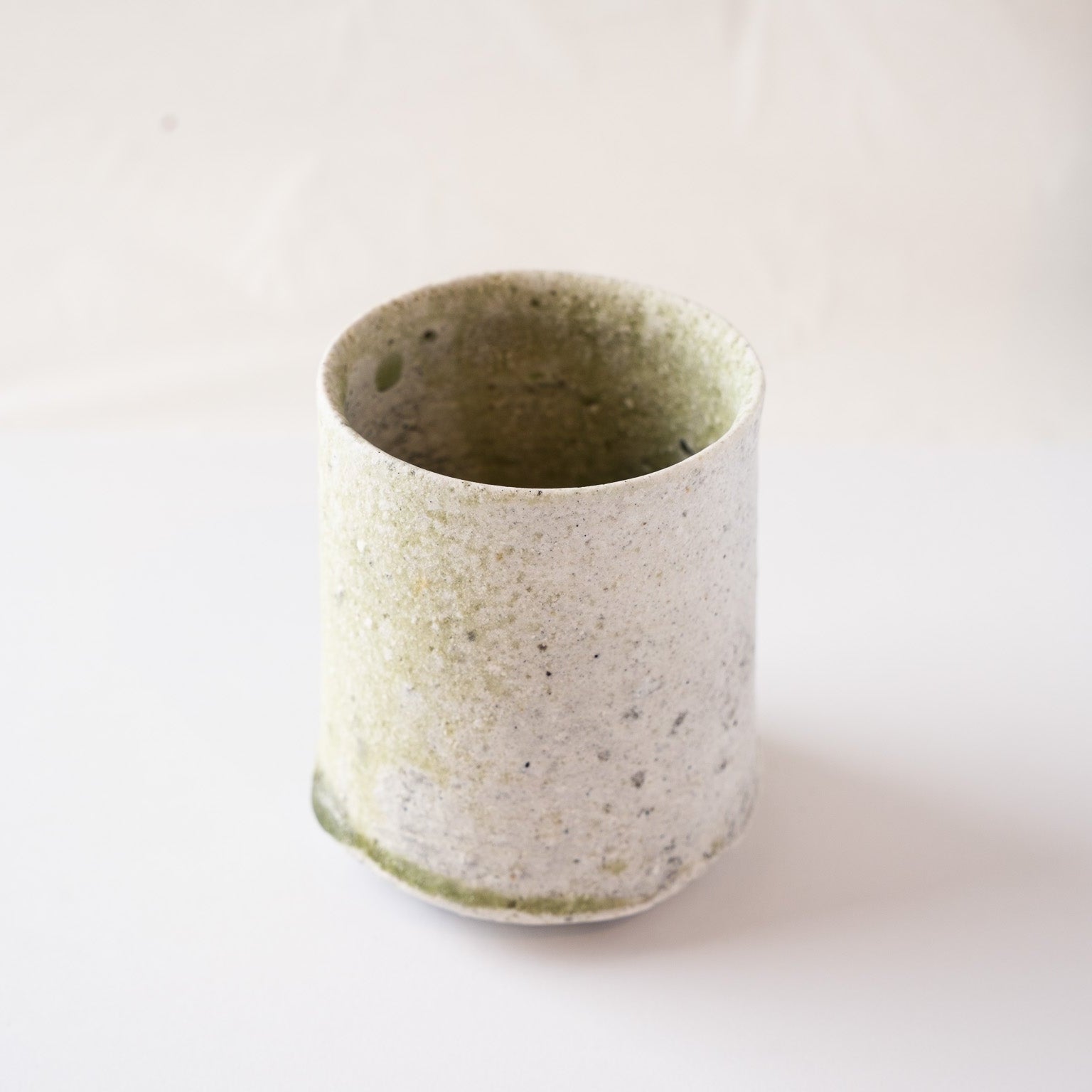 Three-quarter view from the white side of Yui Tsujimura's YUNOMI cup, highlighting the understated elegance and earthy texture of the vessel's rim.