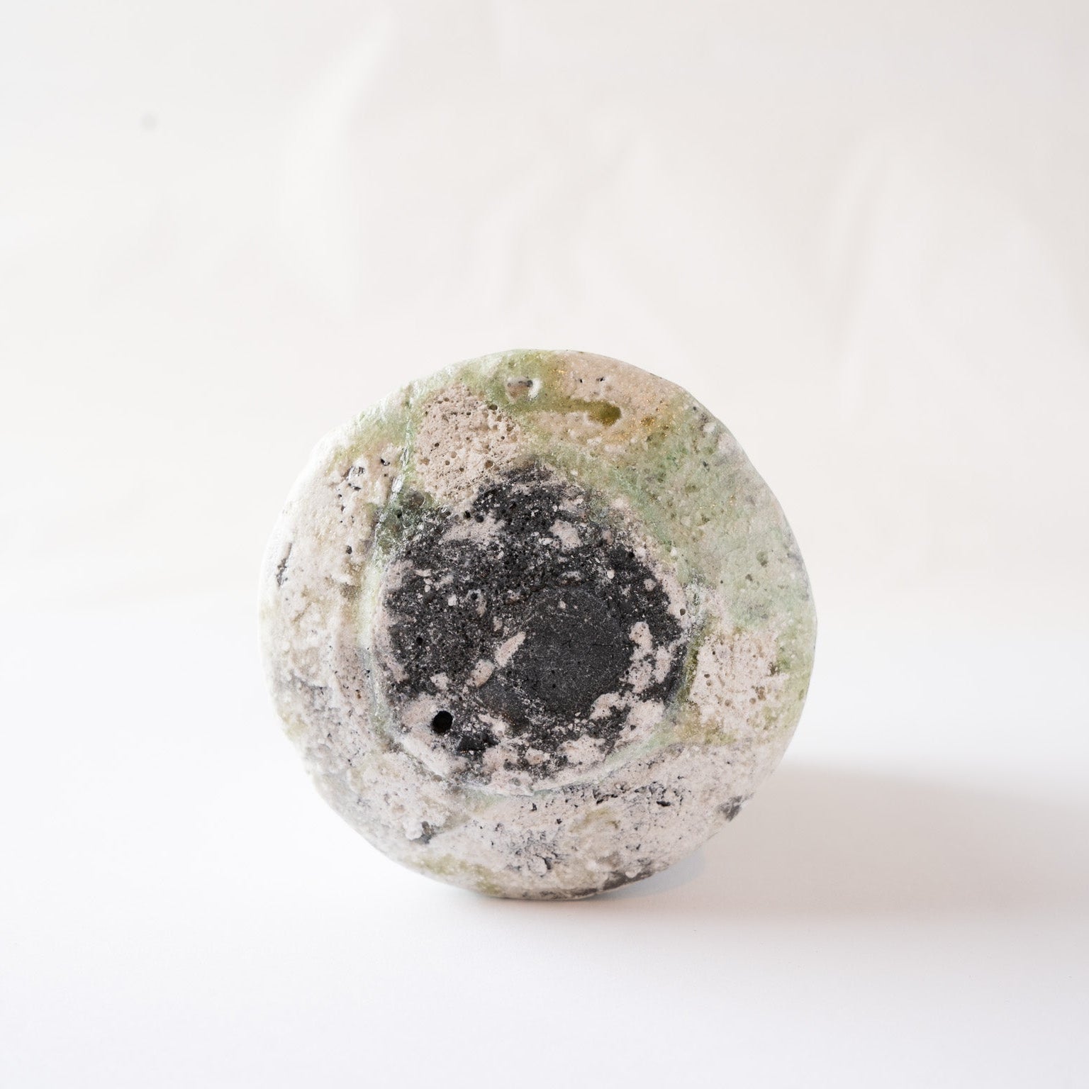Underneath view of the circular base, showing a dark scorch mark in the center surrounded by patches of fused green vidro glaze.