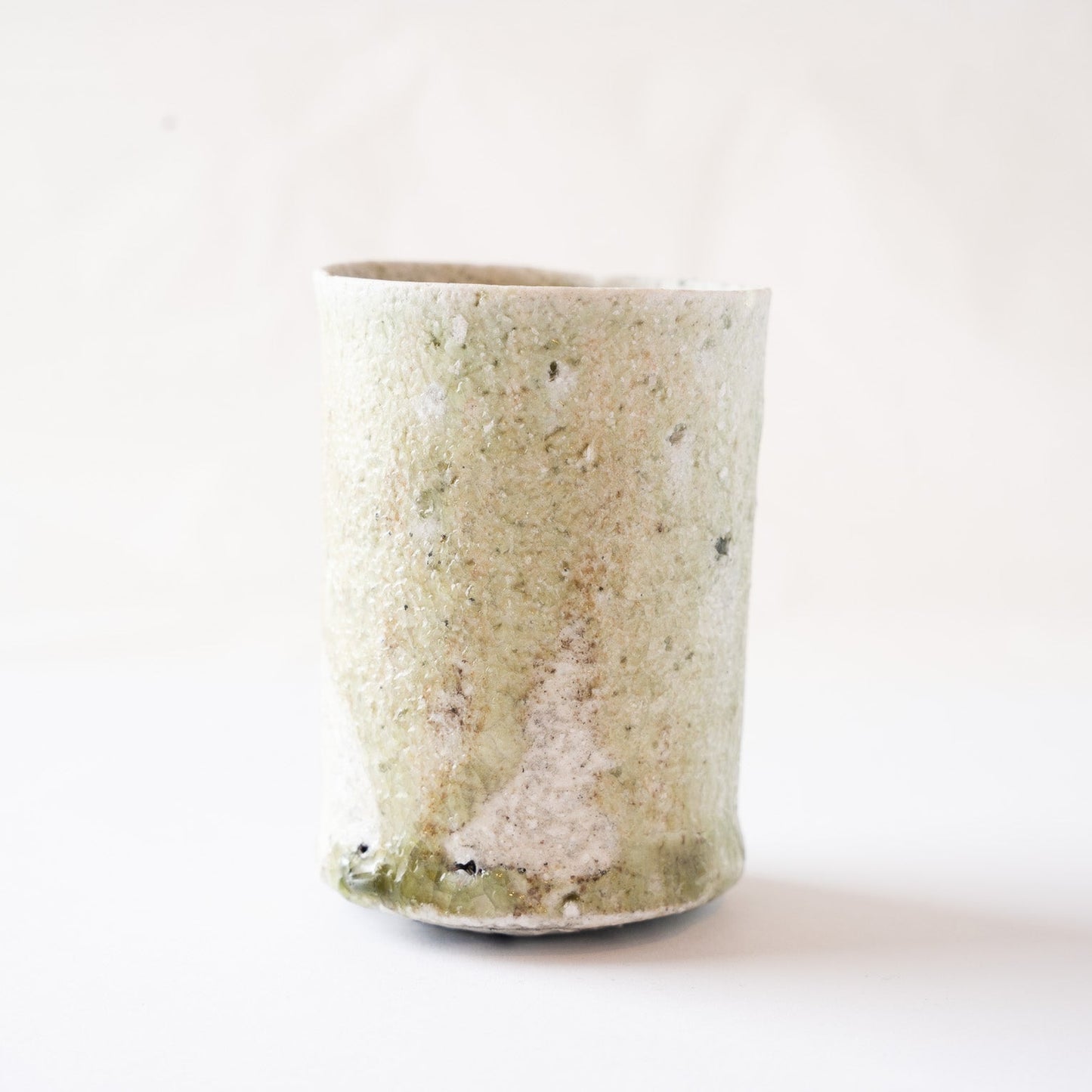 Rotated view of the wood-fired YUNOMI cup showing a soft white ash deposit on the surface and the rich green vidro pool melting near the base.