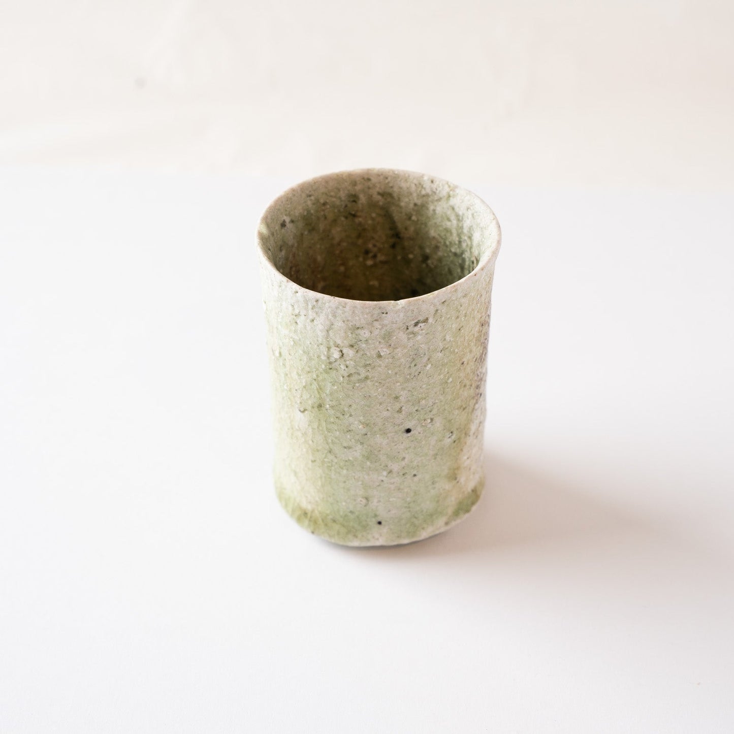 High-angle perspective showing the greenish side of the YUNOMI cup, emphasizing its organic, earth-toned silhouette.