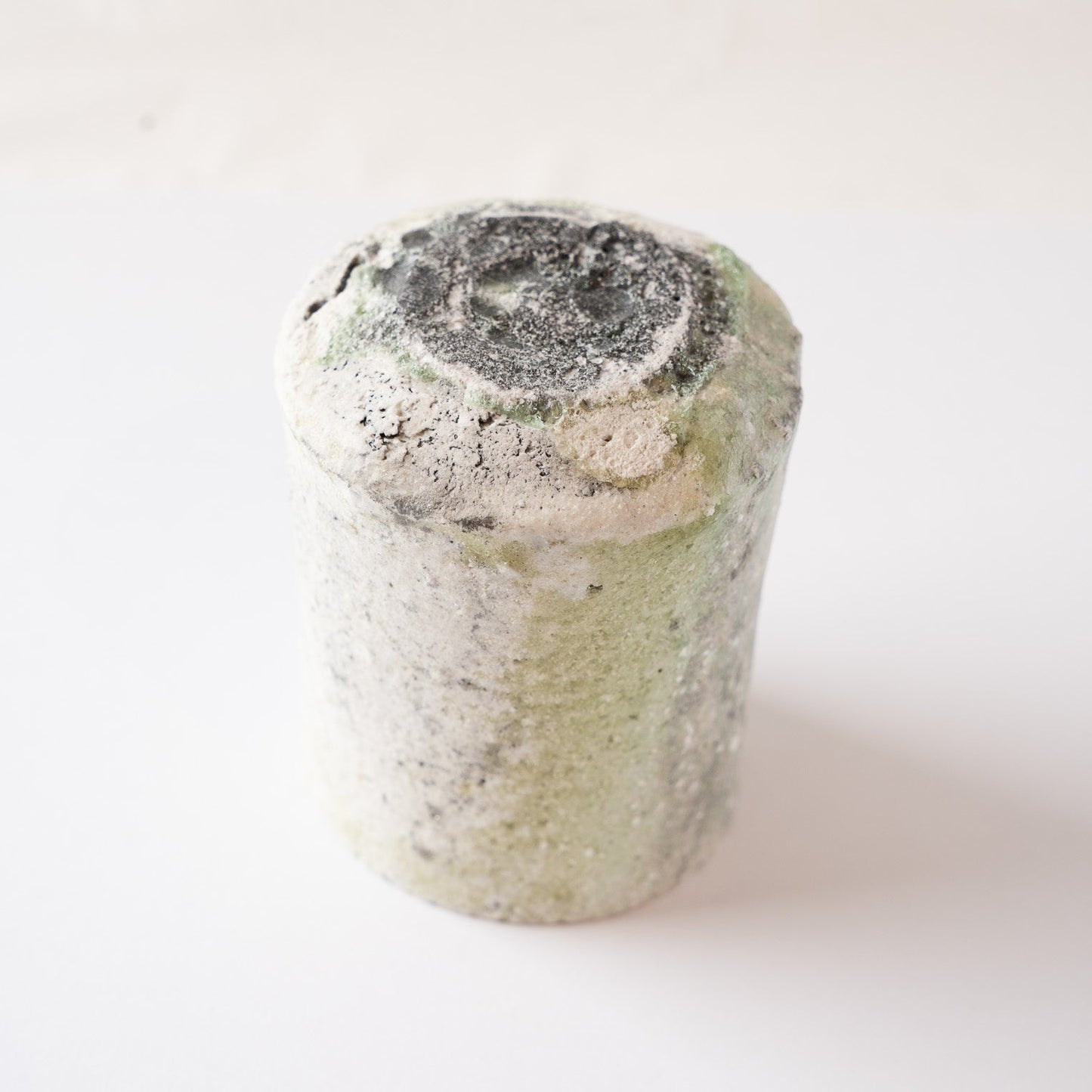 Inverted view of the YUNOMI cup showcasing the heavily sculpted base with dark scorch marks and melted black-green natural glaze formations.
