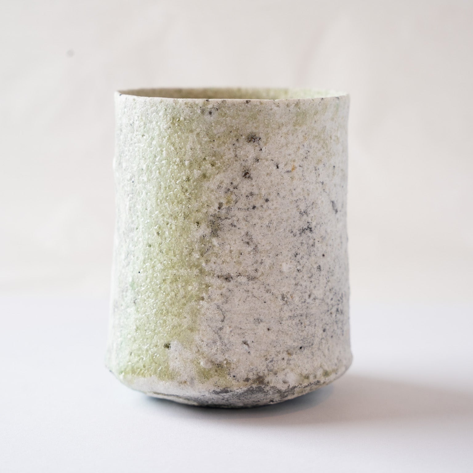 Direct side profile of the YUNOMI cup showing the vertical form and the rough, tactile contrast of the green ash glaze alongside white deposits.