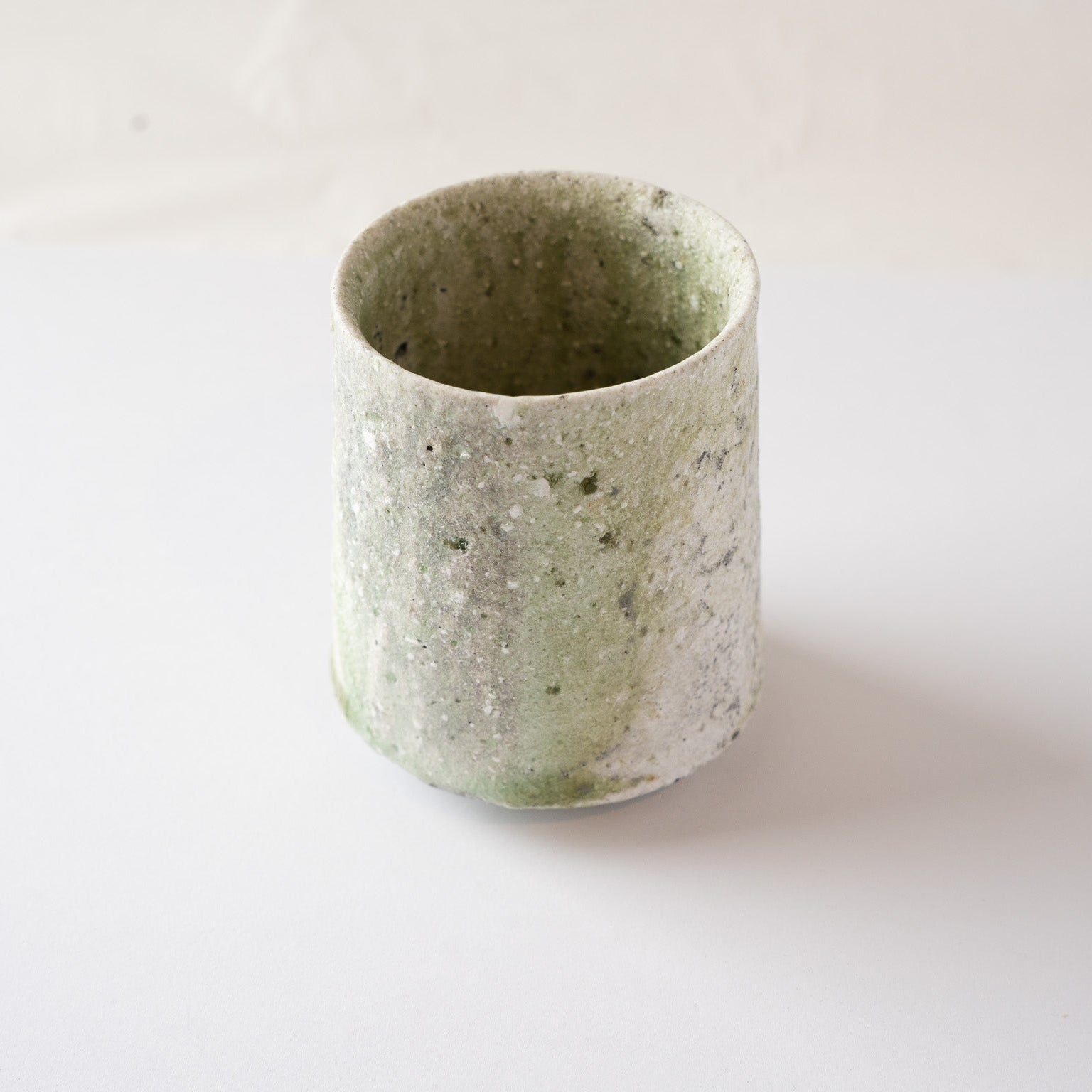 Turned view of the ceramic cup showing the fluid movement of the pale green ash glaze flowing vertically down the side.
