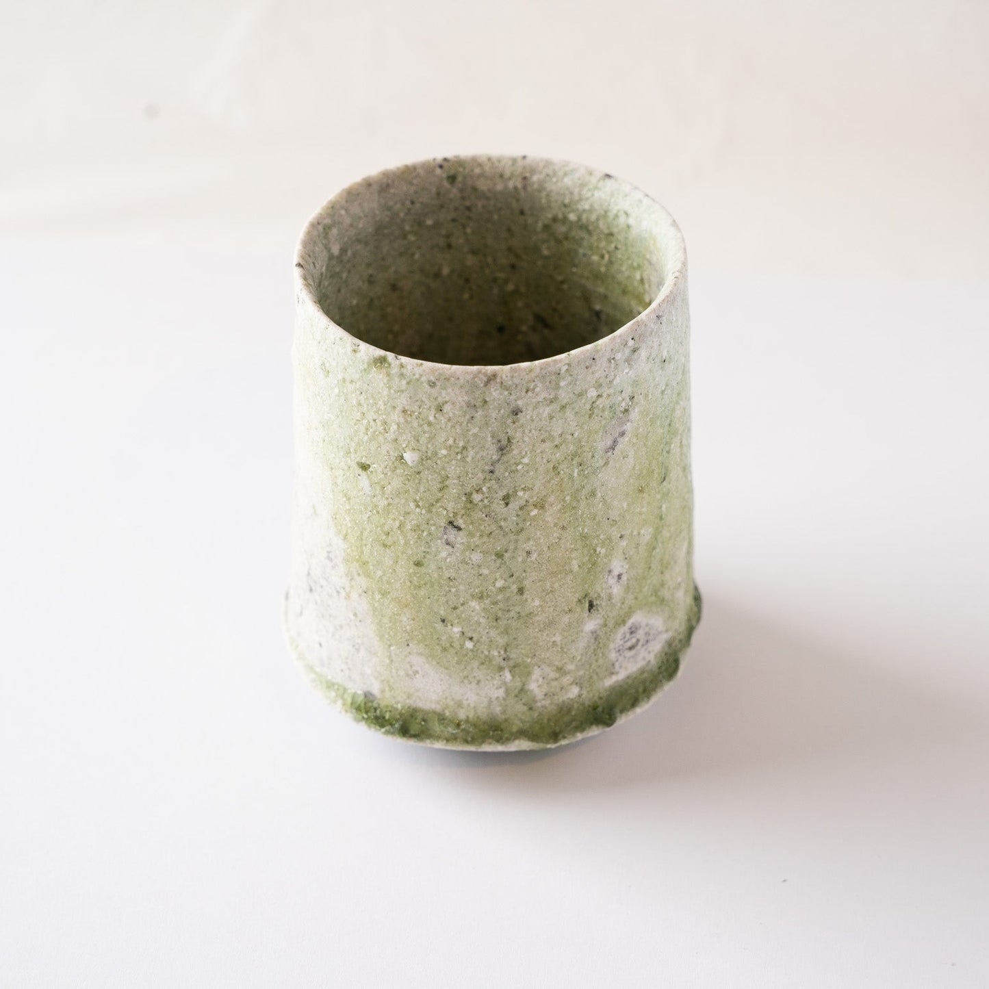 Full side profile of the ceramic YUNOMI cup by Yui Tsujimura, demonstrating the striking vertical contrast of kiln-fired green glaze running down the cylinder form.