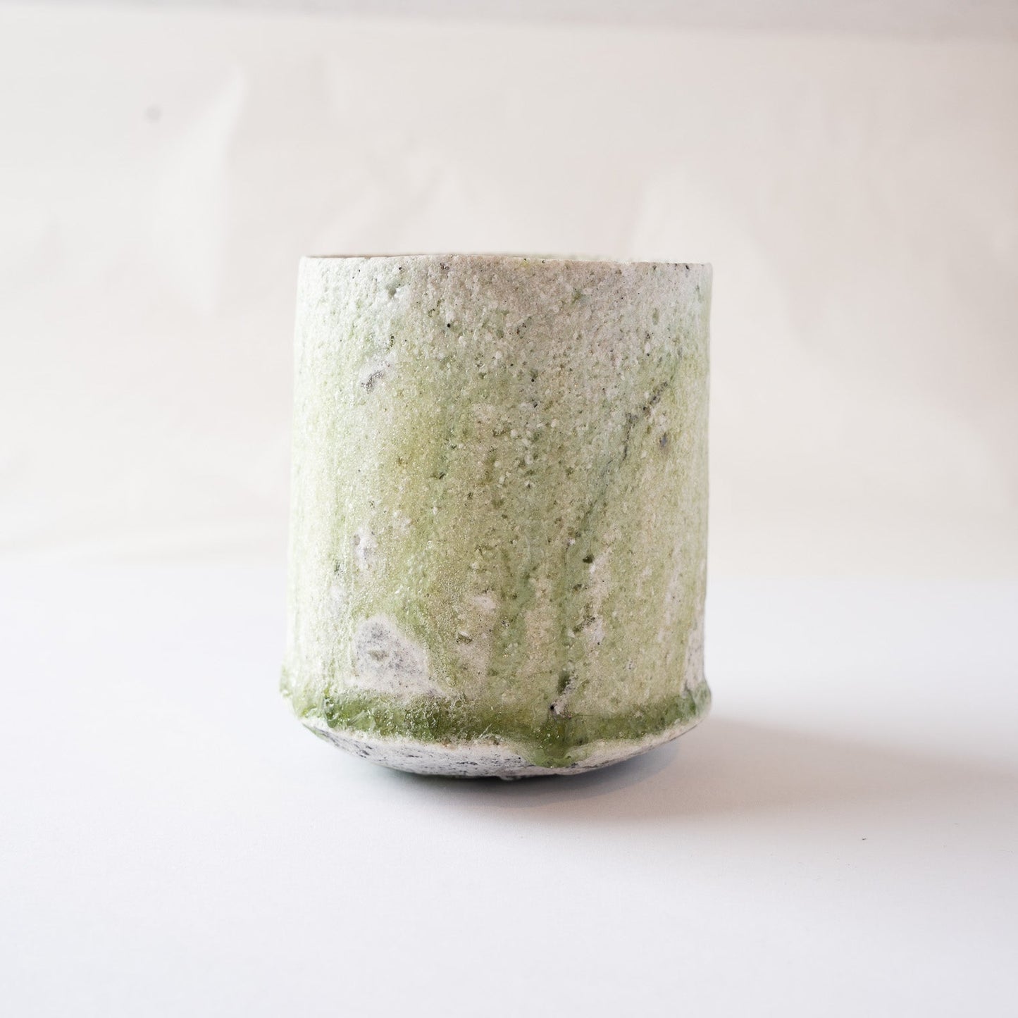 Detailed profile view of the fluid green glaze drips running down to meet the glass ring along the bottom edge of the vessel.