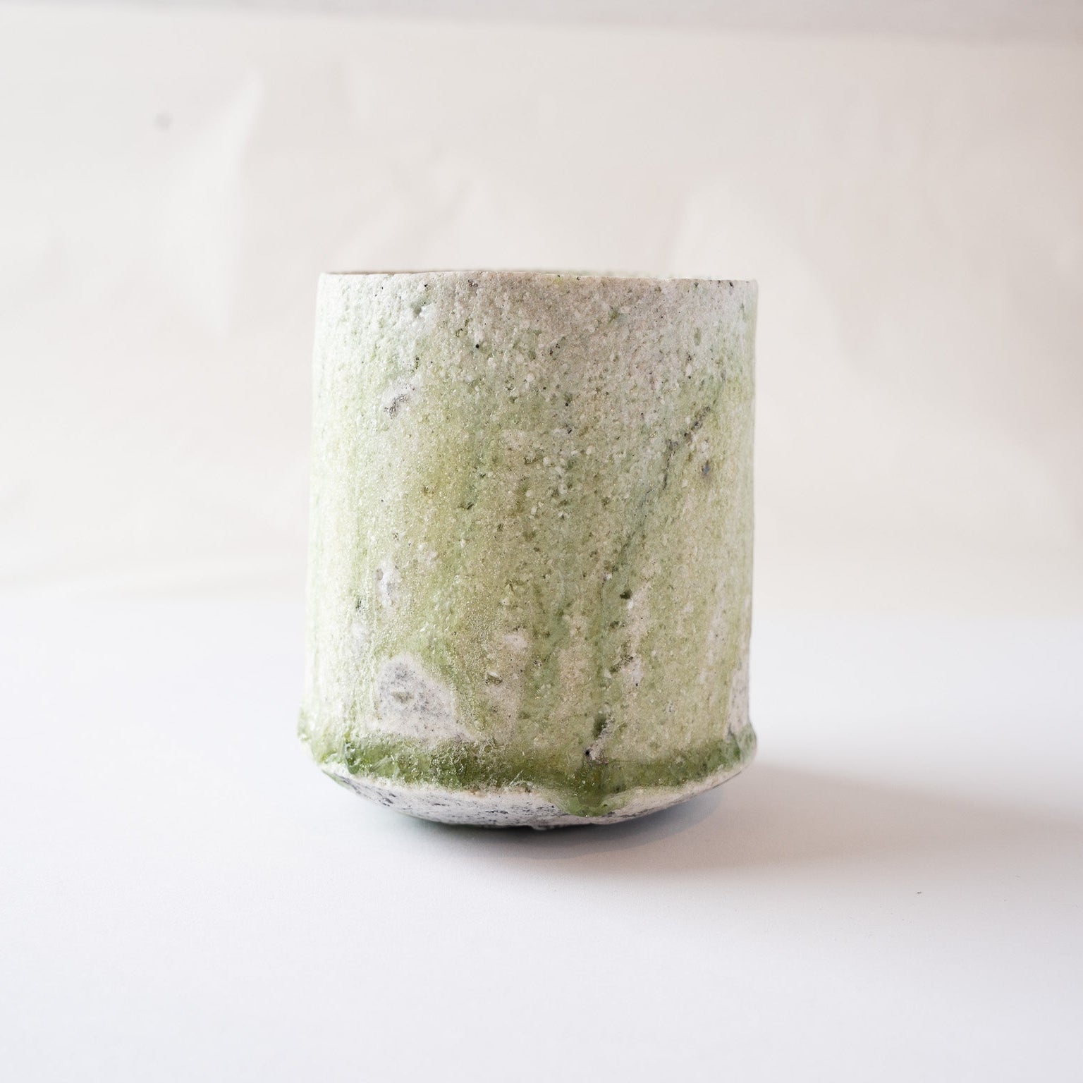 Detailed profile view of the fluid green glaze drips running down to meet the glass ring along the bottom edge of the vessel.