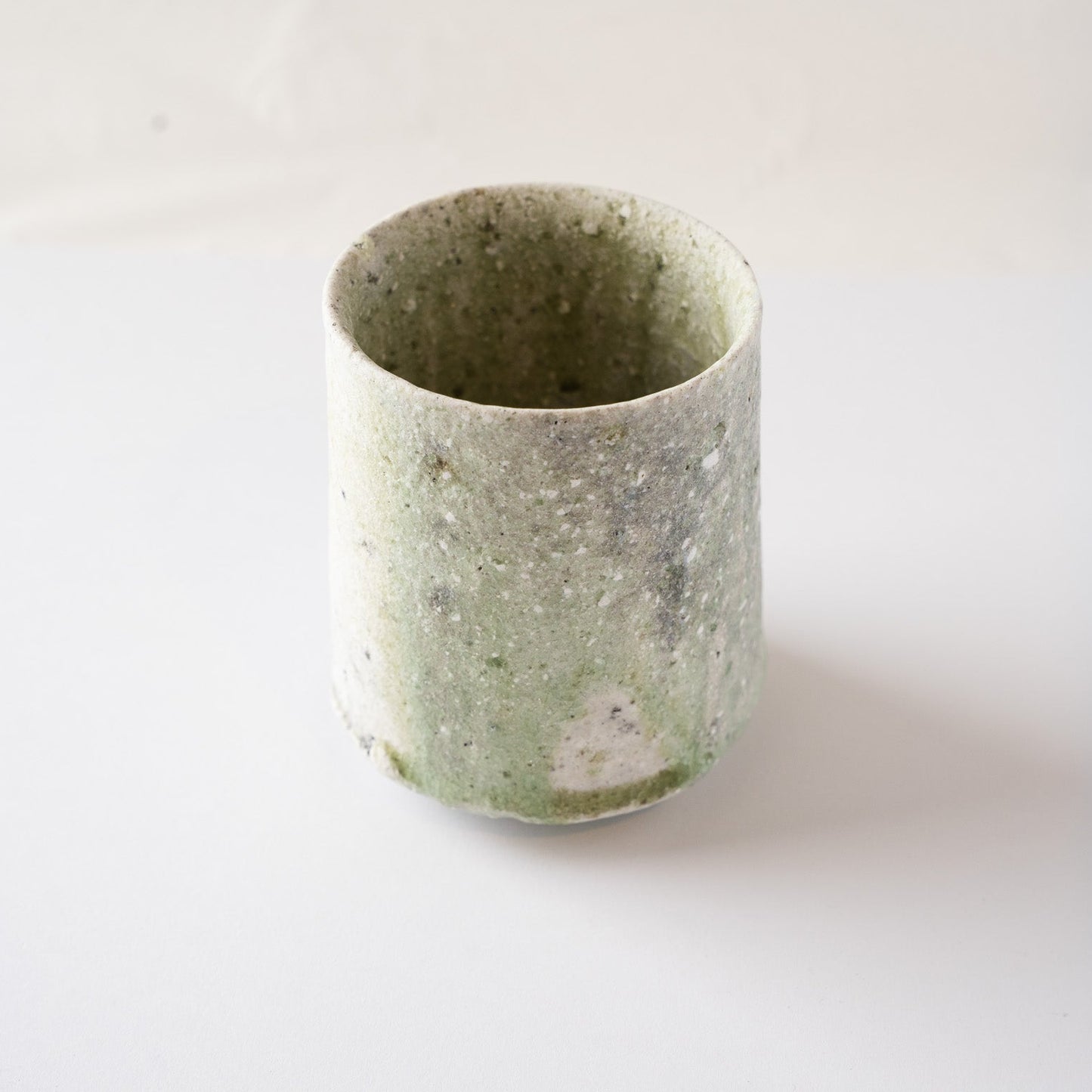 Close-up view highlighting the vibrant, translucent band of deep green vidro glaze accumulated along the lower rim of the cup.