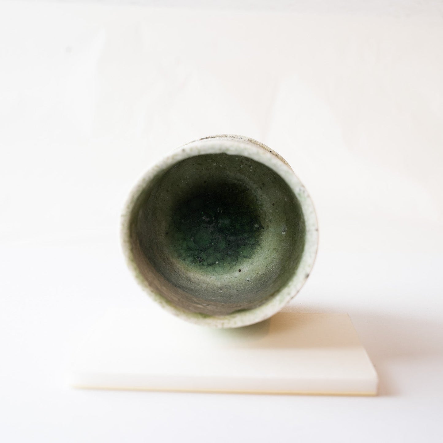 Top-down interior view of the wood-fired YUNOMI cup by Yui Tsujimura, revealing a deep pool of crackled emerald-green glass at the bottom.