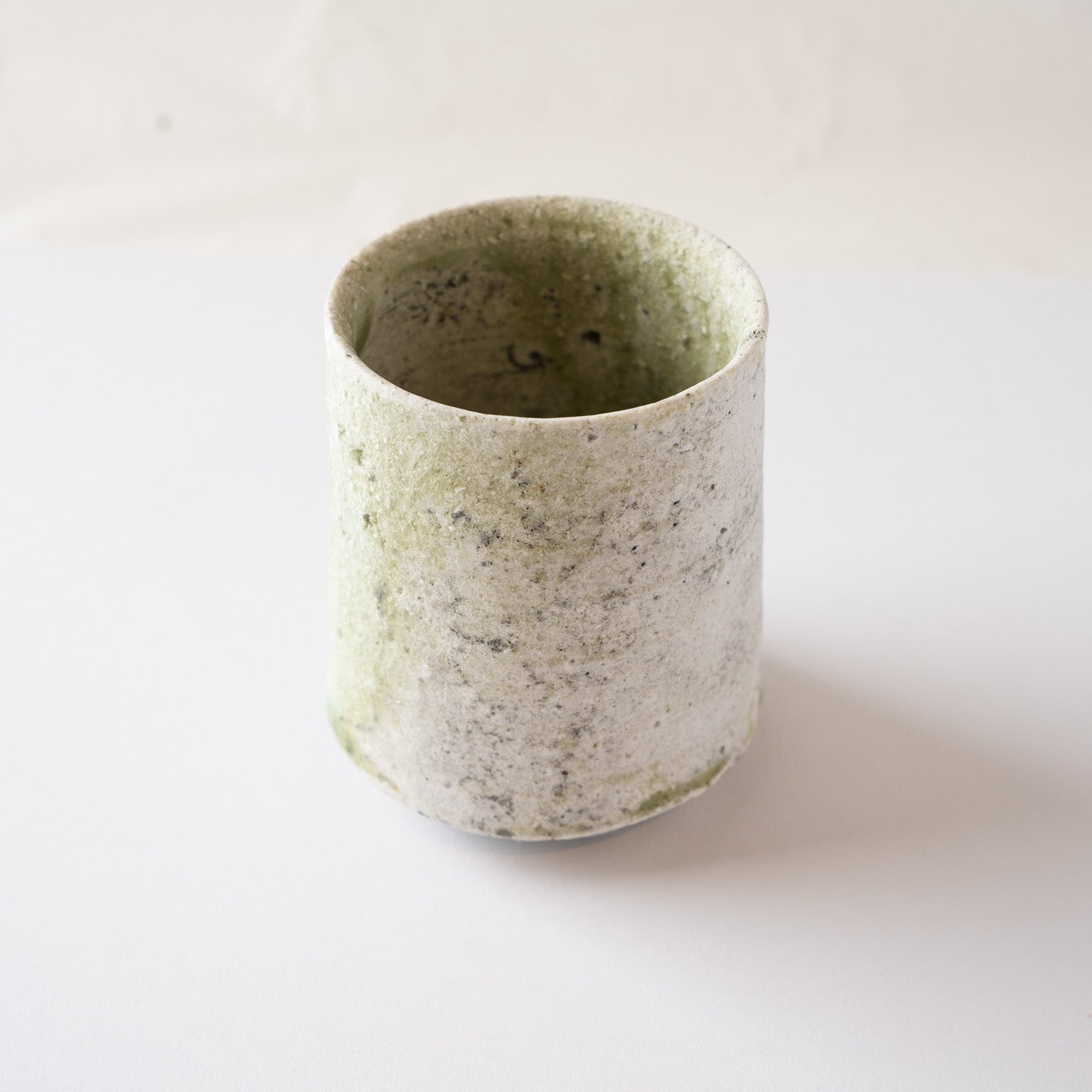 High-angle view of a cylindrical natural glaze YUNOMI cup by Yui Tsujimura, showing a widespread misty pale green vidro glaze over a white ash-textured body.