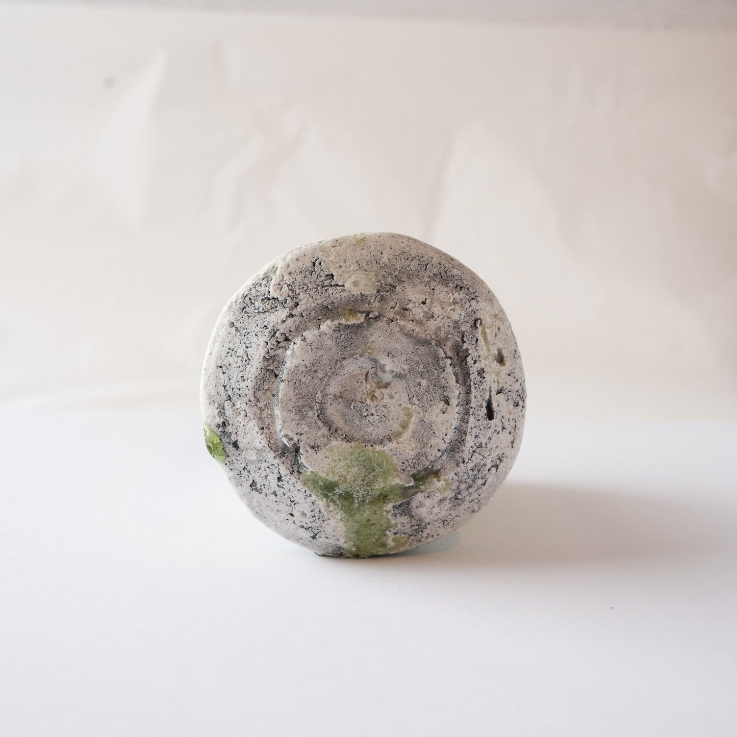 Inverted base view of the ceramic YUNOMI cup by Yui Tsujimura, displaying the rough, sculpted foot with dark kiln scorch marks and melted green glaze edges.