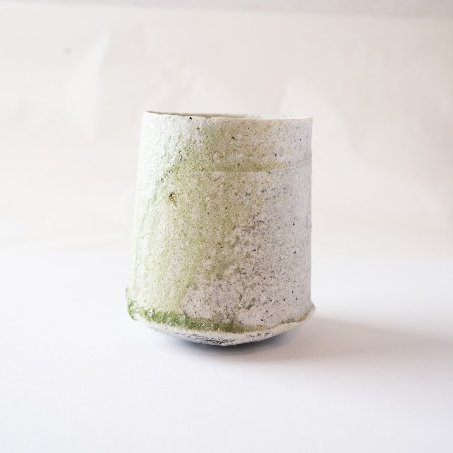 A turned perspective of Yui Tsujimura's natural glaze YUNOMI cup, emphasizing the transition between the vibrant green glaze cascade and the rustic bone-white ash texture.
