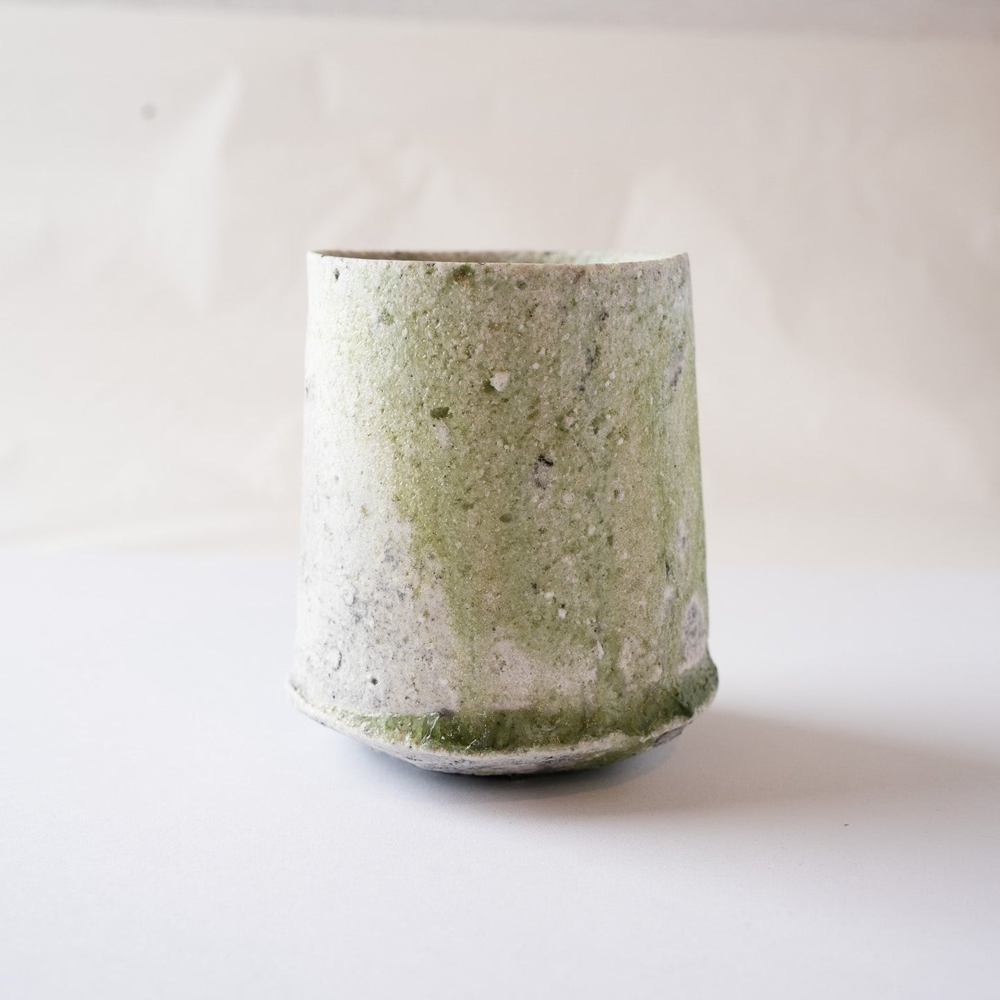 Front profile of a wood-fired ceramic YUNOMI cup by Yui Tsujimura, highlighting a dynamic vertical stream of green vidro ash glaze contrasting against a white crystallized ash surface.