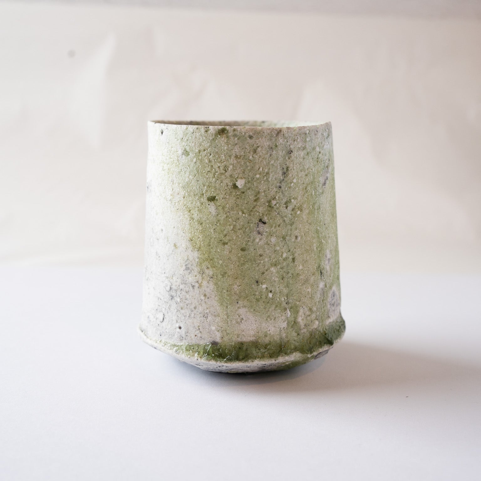 Front profile of a wood-fired ceramic YUNOMI cup by Yui Tsujimura, highlighting a dynamic vertical stream of green vidro ash glaze contrasting against a white crystallized ash surface.