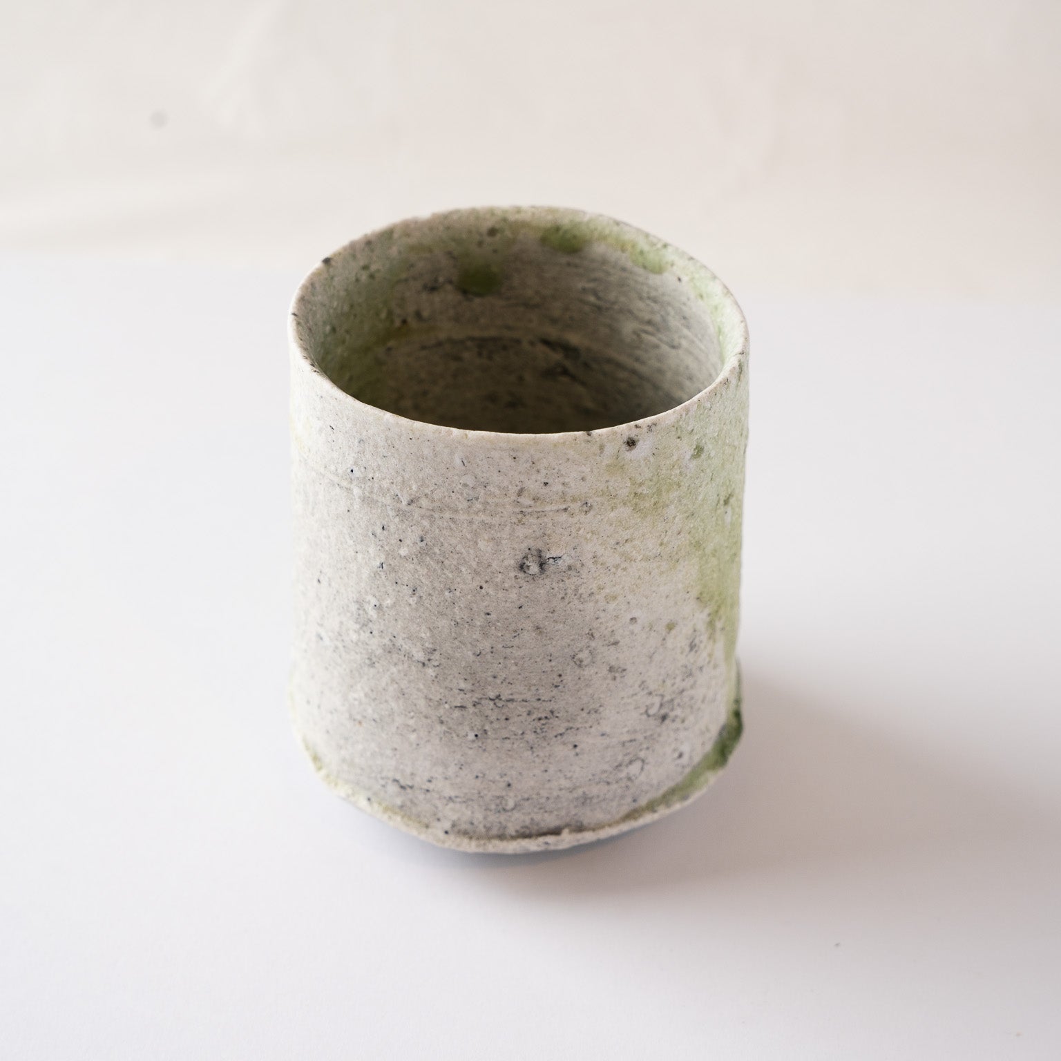 Profile view of the quieter side of the YUNOMI cup by Yui Tsujimura, focusing on the dry, snow-like white crystalline ash deposits.